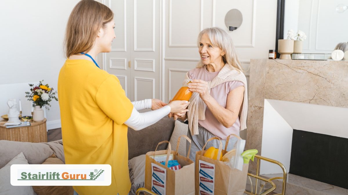 hospital-discharge-home-stairs-featured-v2 Caregiver in a yellow top hands an orange bottle to a smiling elderly woman at home, with grocery bags on a cart nearby.