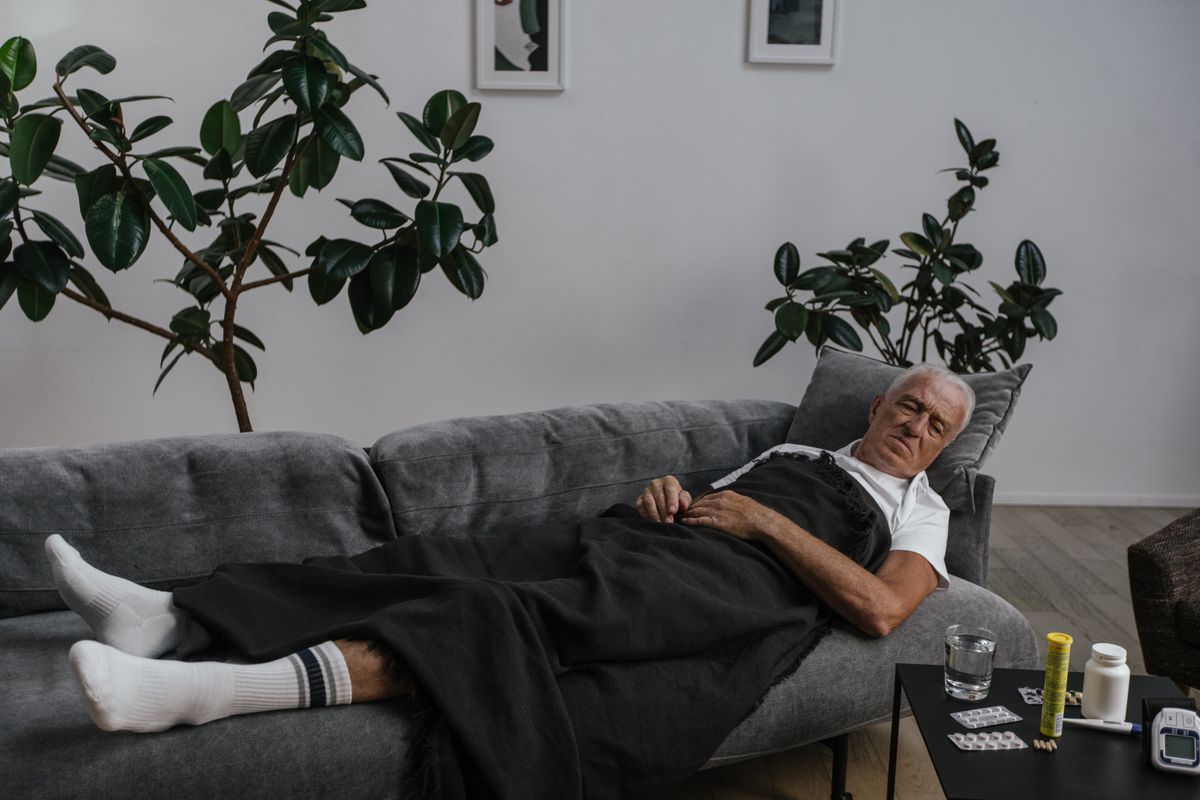 An older man resting on a sofa at home with his medication nearby