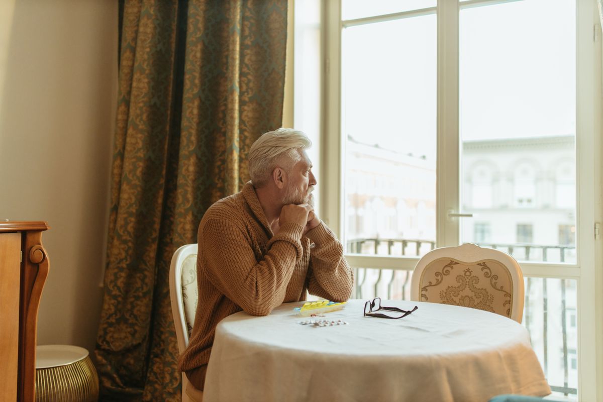 An older man sitting thoughtfully by a window An older man sitting thoughtfully by a window