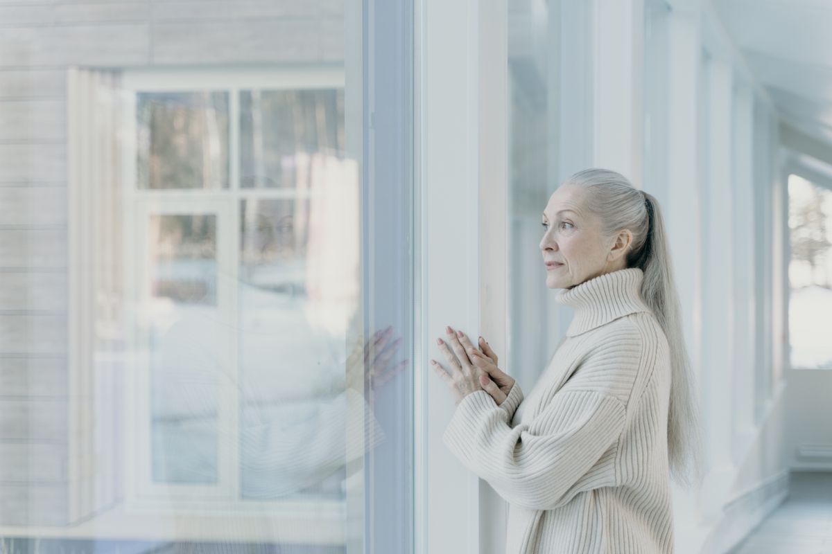 An older woman looking out of a window at home