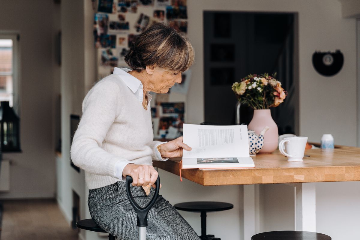 An older woman with a walking stick sitting at a table at home