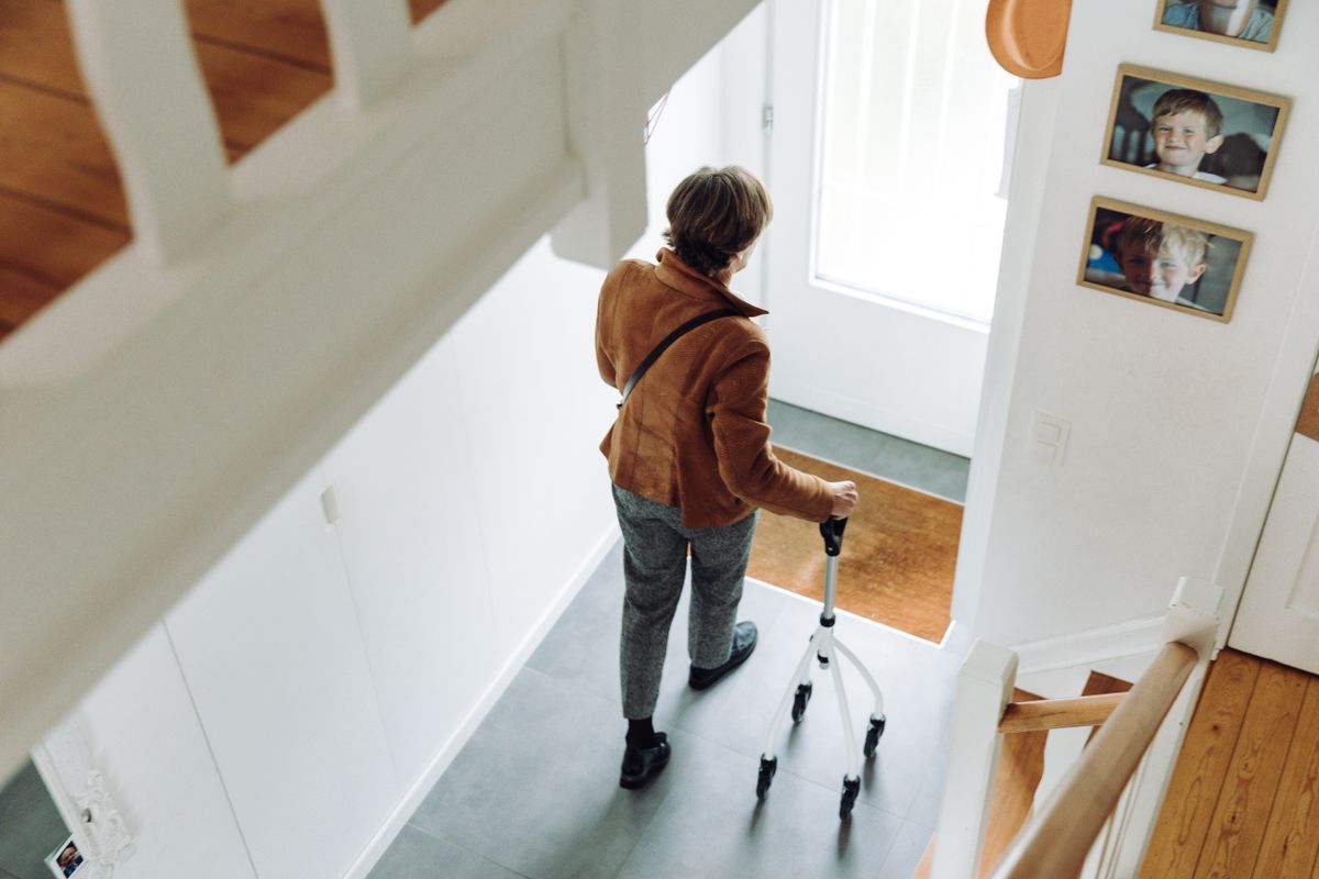 An older person with a walking frame at the foot of a staircase at home An older person with a walking frame at the foot of a staircase at home