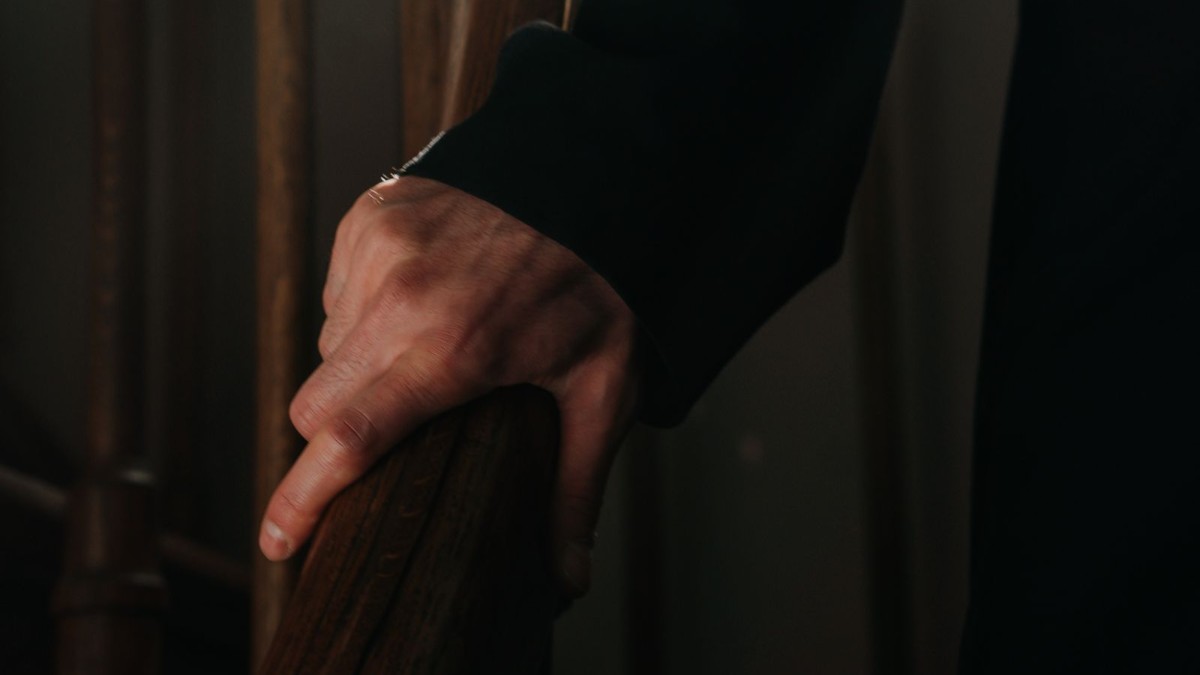 Hand resting on a home stair handrail Close up of a hand resting on a wooden stair handrail at home