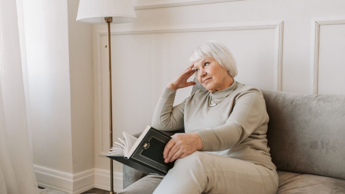 An older woman reading a book on a sofa at home